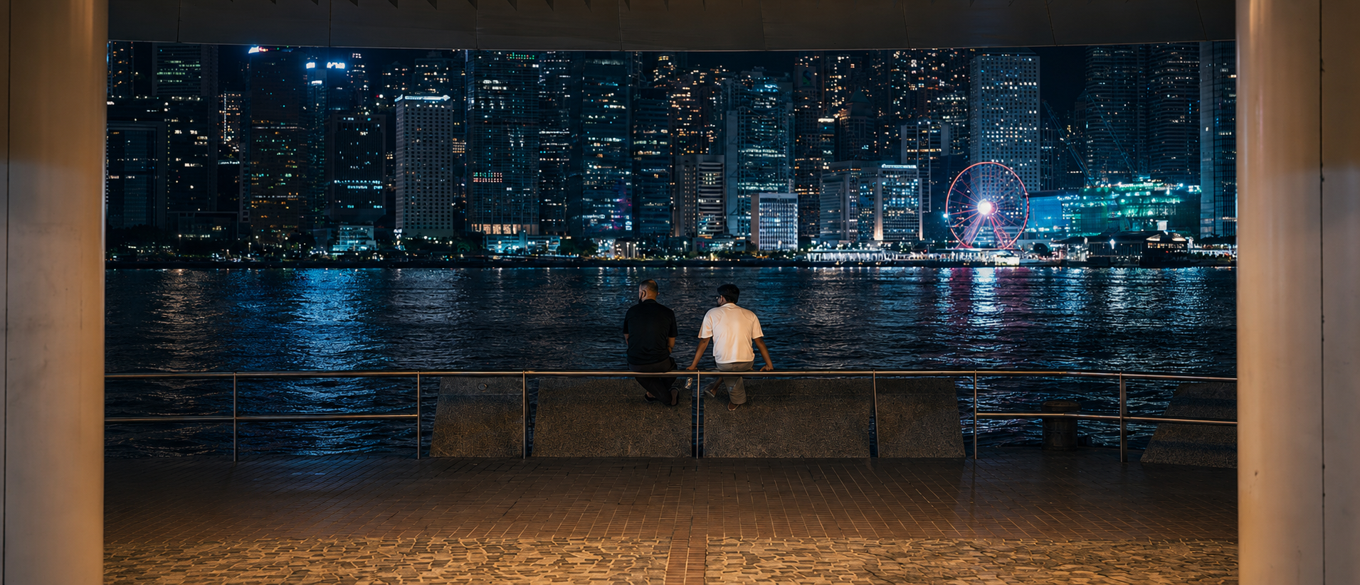 Two people facing the illuminated Hong Kong skyline at night